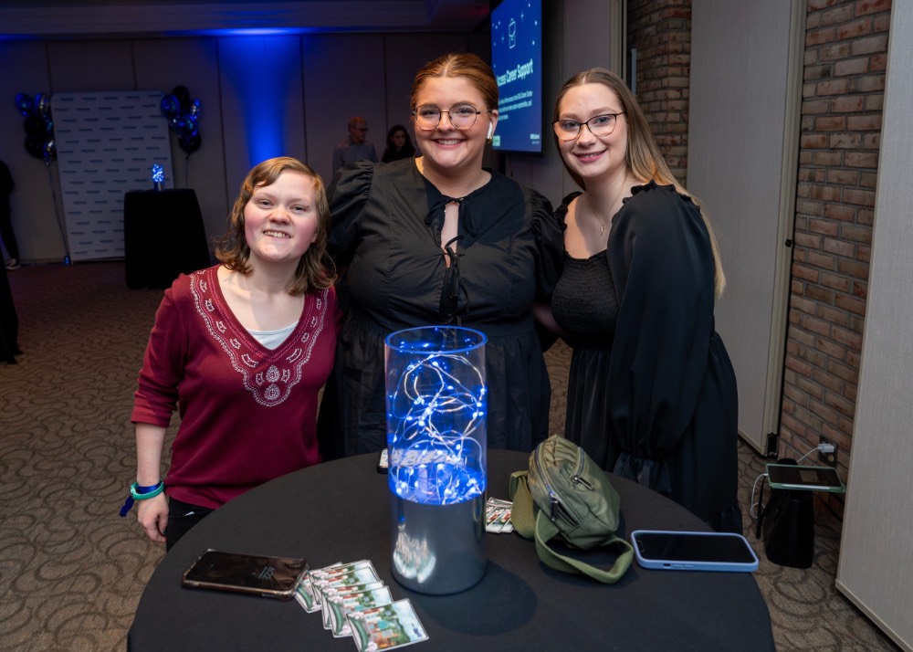 3 girls smiles together around table as they pose